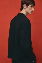 Camisa negra de tejido suave con cuello abierto, tapeta lisa y canesú en la espalda. Modelo de manga larga con cierre ajustable de botones en los puños y tapeta con botón. Bajo recto y corte estándar.