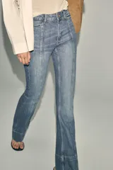 Pantalón de jean azul de tiro alto con nervio marcado delantero, bolsillos delanteros y traseros, bajo acampanado y cierre frontal con cremallera y botón.