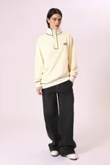 Buzo color crema con cuello alto con botones y ribete negro en cuello, puños y ruedo.