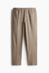 Pantalón jogger de vestir color beige, corte slim fit, con cintura elástica ajustable con cordón, pliegues delanteros y traseros, bolsillos laterales al bies y bolsillos traseros insertados.