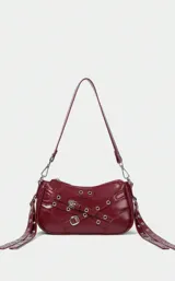 Bolso de hombro pequeño color rojo oscuro (vino) con acabado brillante. Presenta múltiples detalles de estilo 'goth' o 'punk' con correas decorativas, hebillas metálicas y ojales plateados. La correa es delgada y ajustable con mosquetones.
