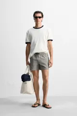 Short de baño con textura seersucker a rayas verticales azul marino y blanco. Tiene cintura elástica ajustable con cordón, bolsillos frontales y traseros, aberturas laterales en el bajo y forro interior.