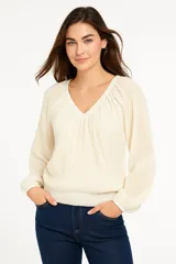Blusa color crema con textura acanalada, escote en V y mangas largas abullonadas con puños elásticos.