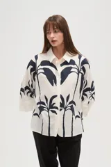 Camisa blanca con estampado de palmeras en color azul marino, de corte holgado, con cuello camisero, cierre frontal con botones y mangas 3/4 con puños anchos.