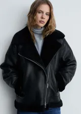 Chaqueta biker negra de efecto piel con cuello de borreguito, cierre de cremallera asimétrico, bolsillos laterales con cremallera y terminaciones de borreguito.