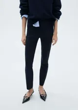 Pantalón skinny negro de tiro medio, con bolsillos laterales y traseros, cierre oculto de botón, gancho y cremallera, y tejido elástico.