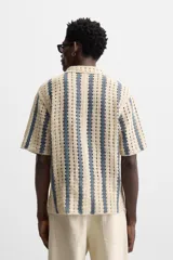 Camisa de crochet color beige con rayas verticales azules, cuello bowling, manga corta y cierre frontal con botones.