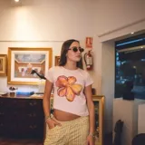 Remera de algodón color rosa claro, de corte cropped y manga corta. Presenta un estampado de una flor de color naranja y amarillo pintada a mano.