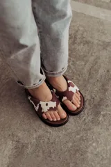 Sandalias tipo ojotas con base acolchada y estampado animal print de vaca en marrón y blanco.