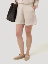 Short de tiro alto color beige con finas rayas verticales blancas. Presenta bolsillos laterales y cierre invisible.