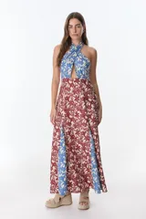 Vestido largo con estampado floral en tonos rojo, azul y beige. Presenta escote halter cruzado con abertura en el pecho y falda acampanada.