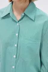 Camisa a rayas verticales verdes y blancas, de corte holgado, manga larga con puños abotonados, cuello clásico y bolsillo de parche en el pecho.