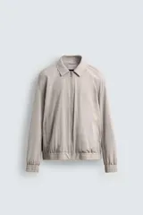 Cazadora bomber color beige claro, de tejido técnico ligero, con cuello solapa, manga larga, bolsillos de vivo en cadera, bolsillo interior, acabados en rib y cierre frontal con cremallera.