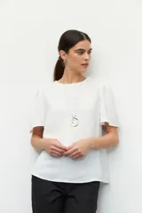 Blusa blanca de mangas cortas abullonadas con botones decorativos en los hombros y textura arrugada.