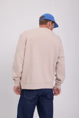 Buzo color beige de manga larga y cuello redondo con logo pequeño en el pecho. Corte relajado y tejido de bucle.