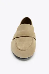 Zapato mocasín color beige de serraje con detalle de tira en la parte delantera y acabado en punta redonda.