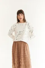 Sweater color beige de tejido de punto con cuello redondo y mangas largas. Presenta apliques de lentejuelas plateadas en el frente y las mangas.