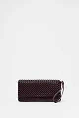 Bolso alargado color borgoña con diseño trenzado, asa bandolera y tirador con pulsera de mano. Incluye bolsillo interior, cierre mediante solapa y botón imantado.