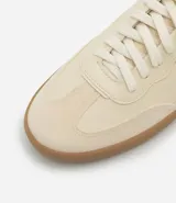 Championes estilo chutera color crema con detalles laterales y traseros en negro. Suela plana color caramelo y cierre con cordones. Confeccionados en poliuretano y poliéster.