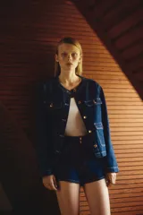 Campera de denim azul con cuello redondo, cierre frontal con botones dorados y cuatro bolsillos de parche con solapa y botón.