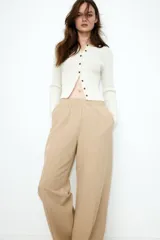 Pantalón color beige de lino con tiro alto, cintura elástica, bolsillos al bies y bolsillos traseros insertados. Piernas rectas con pliegue cosido adelante.