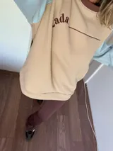 Buzo color beige con mangas celeste pastel y puños y ruedo acanalados.