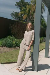 Conjunto de camisa de manga corta con cuello y pantalón de corte recto, ambos de tela simil lino color beige con bordados blancos.