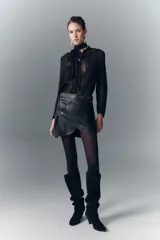 Minifalda negra de cuero ovino con cinturón fijo, remaches decorativos y arandelas metálicas.