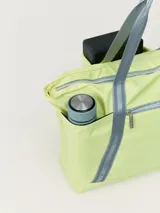Bolso tipo tote de poliéster color verde oliva con asas de cinta negra. Tiene cierre superior y seis bolsillos externos, uno con ajuste elástico y otro con cremallera.