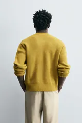 Chaqueta de punto color mostaza, corte relaxed fit, con cuello elástico, manga larga, bolsillos en la cadera, acabados en rib y cierre frontal con cremallera.