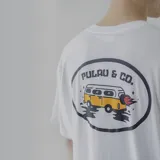 Remera blanca de algodón con estampa en la espalda de una combi amarilla con llamas saliendo del escape, dentro de un óvalo con el texto "Pulau & Co.".