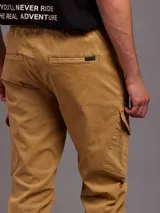 Pantalón cargo color ocre de sarga, con cintura elástica ajustable con cordón, bolsillos laterales con cierre y bolsillos cargo con solapa en los muslos.