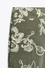 Pantalón de tiro alto color verde oliva con bordado floral blanco, bolsillos laterales ocultos, pernera ancha y terminación en guipur.