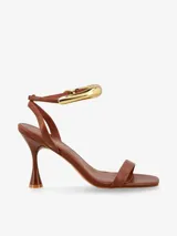 Sandalias de tacón negras con tira delgada sobre los dedos y pulsera tobillera con adorno tubular plateado.
