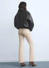 Pantalón de jean color beige claro, tiro medio, estilo campana (flare) con bajo deshilachado y cinco bolsillos.