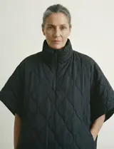 Poncho acolchado color mostaza con cuello alto y abertura frontal con cierre. Presenta un patrón capitoné de formas ovaladas y bolsillos delanteros.