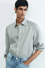Camisa de lino color gris con cuello inglés, tapeta clásica, canesú en la espalda, mangas largas con tapeta de manga y botón, cierre ajustable de botón en los puños y bajo redondeado.
