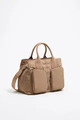 Bolso bandolera color beige de nylon con detalles de cuero. Tiene doble asa de mano, correa bandolera ajustable y extraíble, dos bolsillos frontales con cierre y logo metálico de la marca.