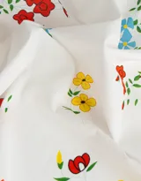 Pañuelo cuadrado de algodón color blanco con estampado de flores rojas, azules y amarillas, y ribete ondulado rojo.