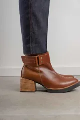 Bota corta de cuero marrón con puntera redondeada y taco cuadrado. Presenta una correa con hebilla alrededor del tobillo y cierre lateral.