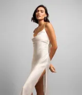 Vestido midi color blanco hueso de satén, con breteles finos, escote drapeado y lazo en la espalda. Presenta una abertura lateral en la falda.