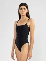 Traje de baño enterizo negro con breteles finos y detalle de cadena dorada en uno de los hombros.