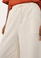 Pantalón de lino color crema, de corte recto y tiro alto, con cintura elástica ajustable con cordón y bolsillos laterales.