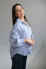 Camisa de manga larga con cuello camisero y escote en pico. Diseño a rayas verticales azules y blancas con bordados florales perforados en blanco en la parte delantera y trasera.