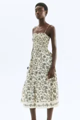 Vestido midi color crudo con estampado de hojas en negro, breteles finos ajustables y escote recto con frunces.