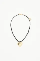 Collar de cadena de cuentas irregulares negras con dije central de corazón texturizado dorado y detalle de piedra negra.