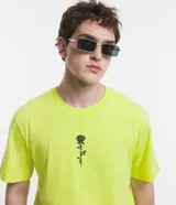 Remera color amarillo flúor de corte recto, con cuello redondo y manga corta. Presenta un bordado de una rosa negra en el lado izquierdo del pecho.