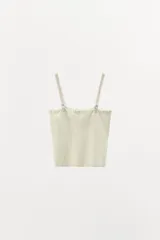 Top de punto color crema claro, corte recto y ajustado, con detalle de encaje floral bordado en el escote. Posee tirantes ajustables de color beige claro.