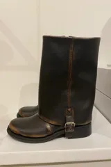 Bota de cuero color marrón oscuro con efecto desgastado, caña media, hebilla lateral y suela plana.