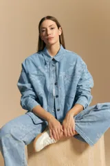 Sobrecamisa de denim celeste con estampado floral tono sobre tono. Presenta cuello camisero, cartera frontal con botones metálicos y bolsillos aplicados en el pecho.